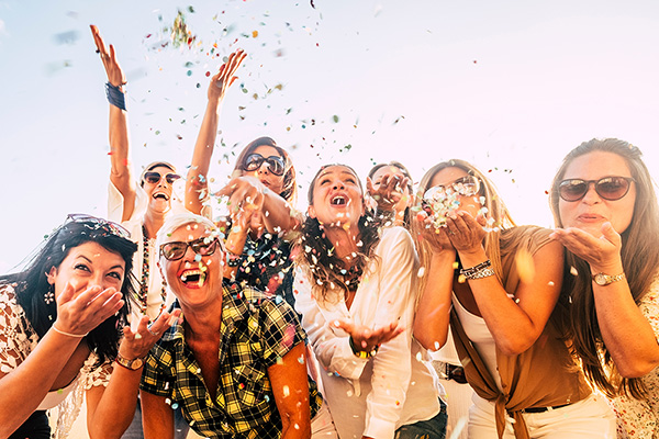 People having fun in party celebration friends concept - group of young and adult women all together laughing blowing coloured confetti - friendship and love for lifestyle with mixed active generations